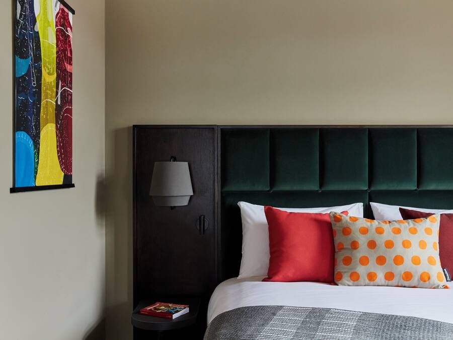 A hotel room with a bed, a nightstand, a lamp, and a colorful artwork on the wall.