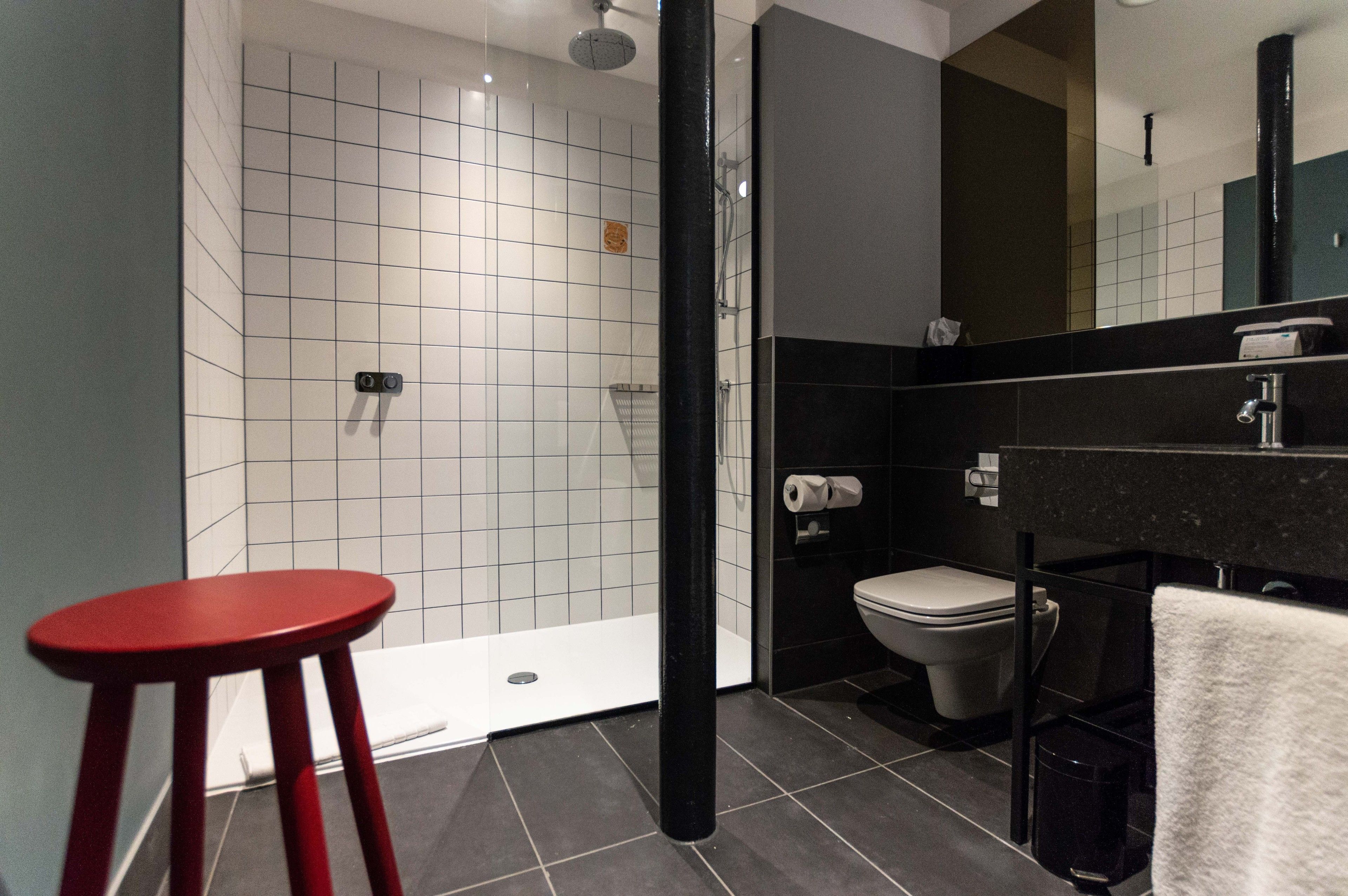 Un baño moderno con ducha, inodoro y un taburete rojo.