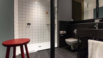 Un baño moderno con ducha, inodoro y un taburete rojo.