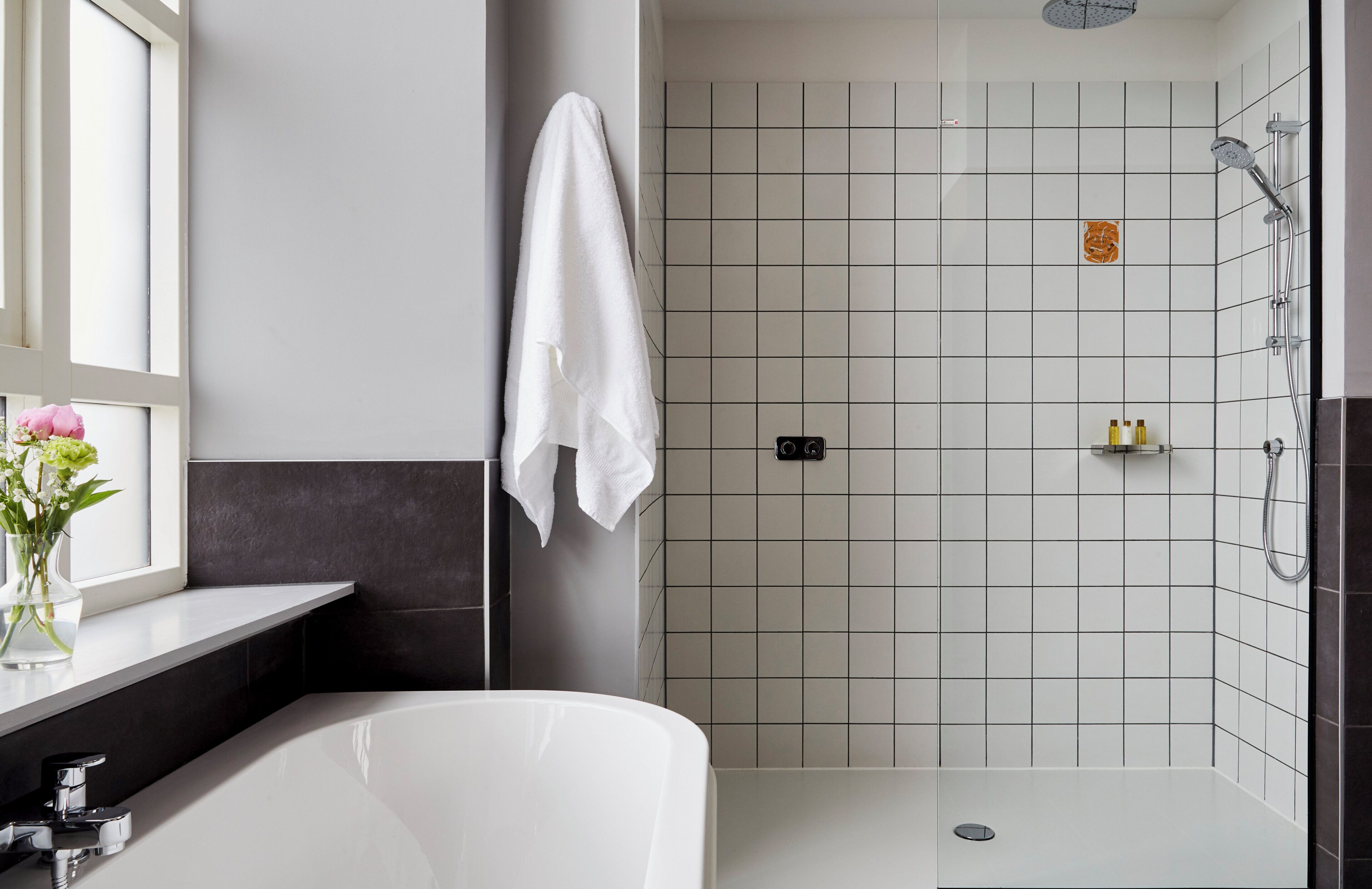 A modern bathroom with a bathtub, a shower area, and a window with flowers.