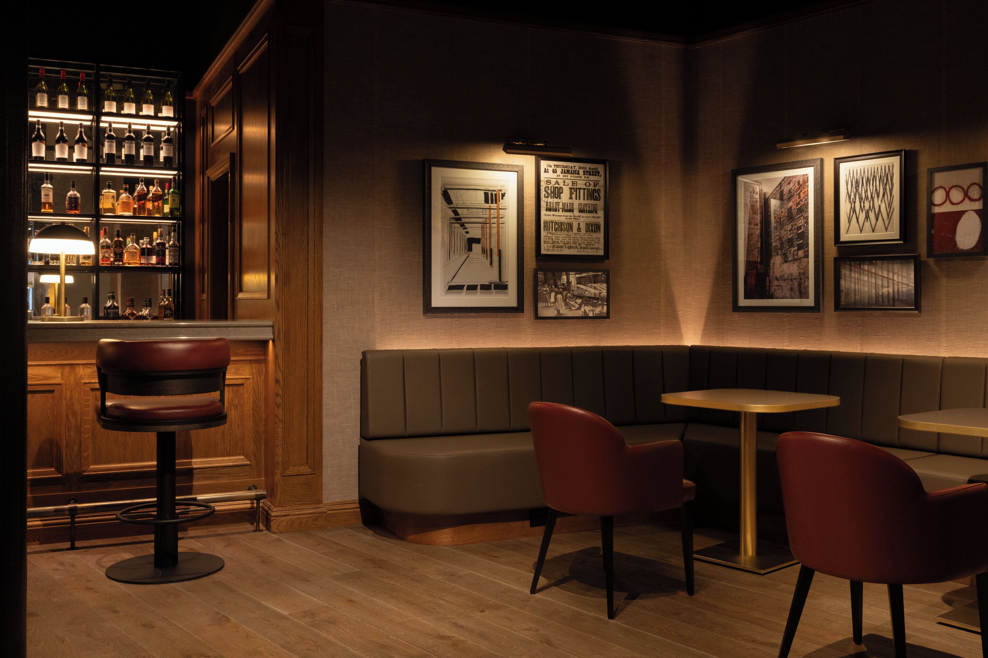 Een bar met een houten toog, een zithoek met een bank en stoelen, en ingelijste foto's aan de muur.