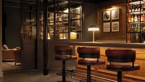 A bar area with stools, a bar counter, and shelves of bottles. - Hotel Indigo Dundee by IHG (Dundee)