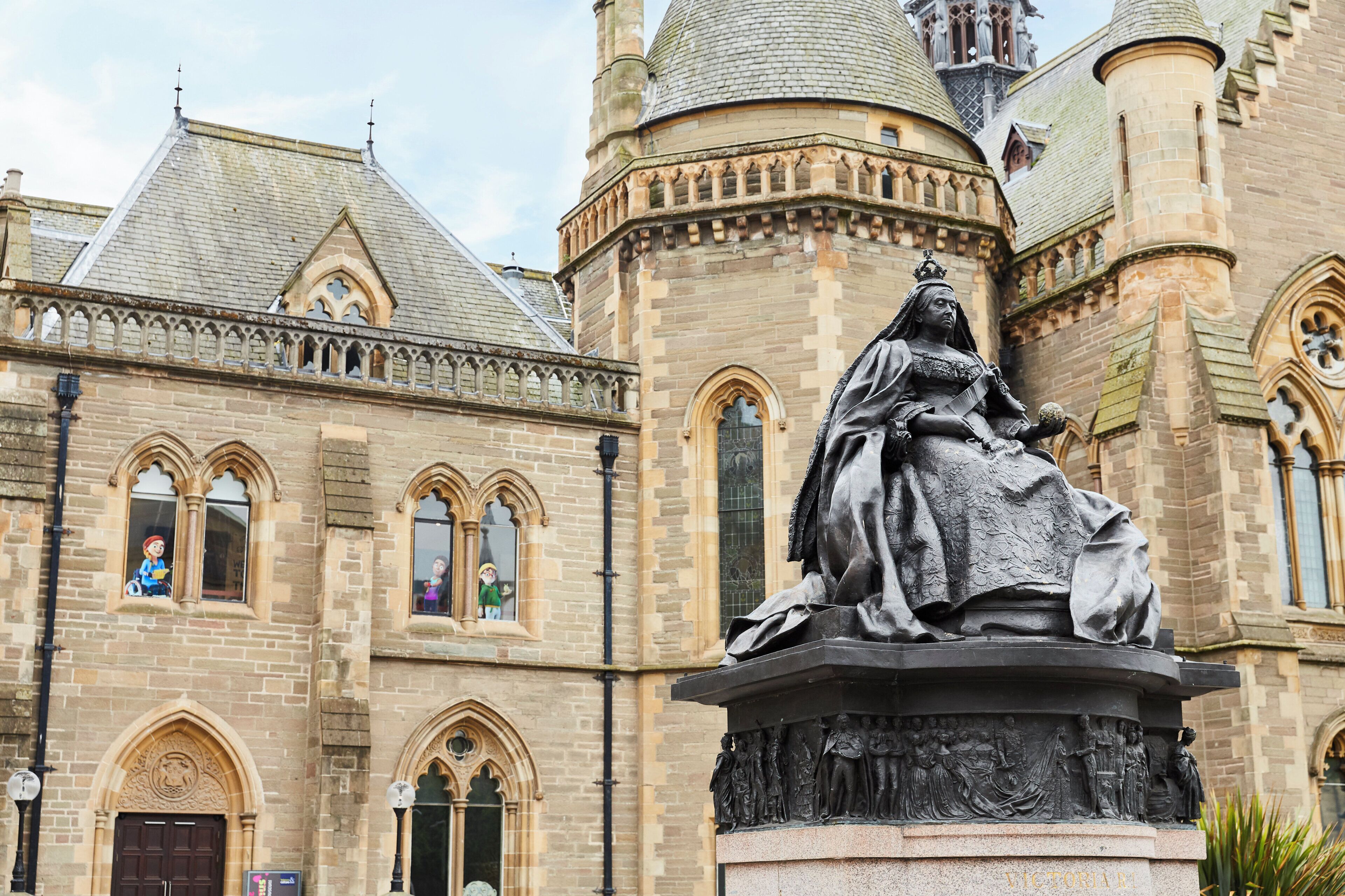 Un bâtiment historique, remarquable par la présence d’une statue imposante représentant une figure assise, des fenêtres en arc de cercle et une tour surmontée d’un dôme.