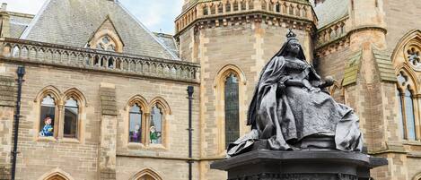 Un bâtiment historique, remarquable par la présence d’une statue imposante représentant une figure assise, des fenêtres en arc de cercle et une tour surmontée d’un dôme.
