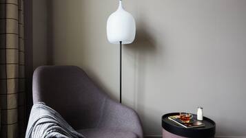Ein modernes Zimmer mit einem grauen Sessel, einer Stehlampe und einem Beistelltisch mit einem Buch und einer Tasse.