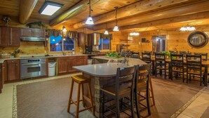 A spacious kitchen with wooden cabinets, a large island with stools, and a dining area with multiple chairs. - Moose Hollow Lodge (Sevierville)
