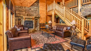 A log cabin interior with a stone fireplace, leather furniture, and a wooden staircase. - Moose Hollow Lodge (Sevierville)