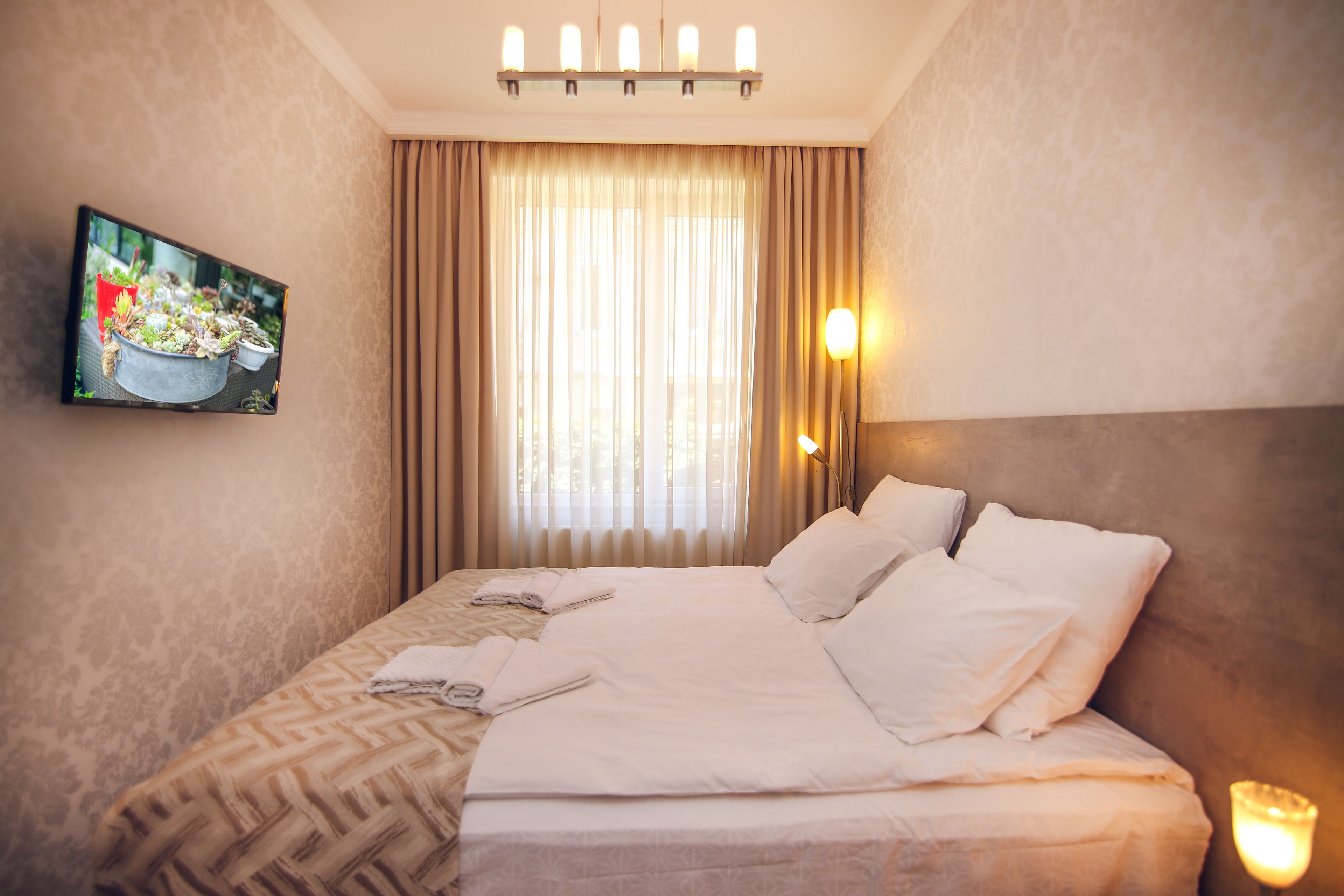 A hotel room with a large bed, a flat-screen TV mounted on the wall, and a window with curtains.