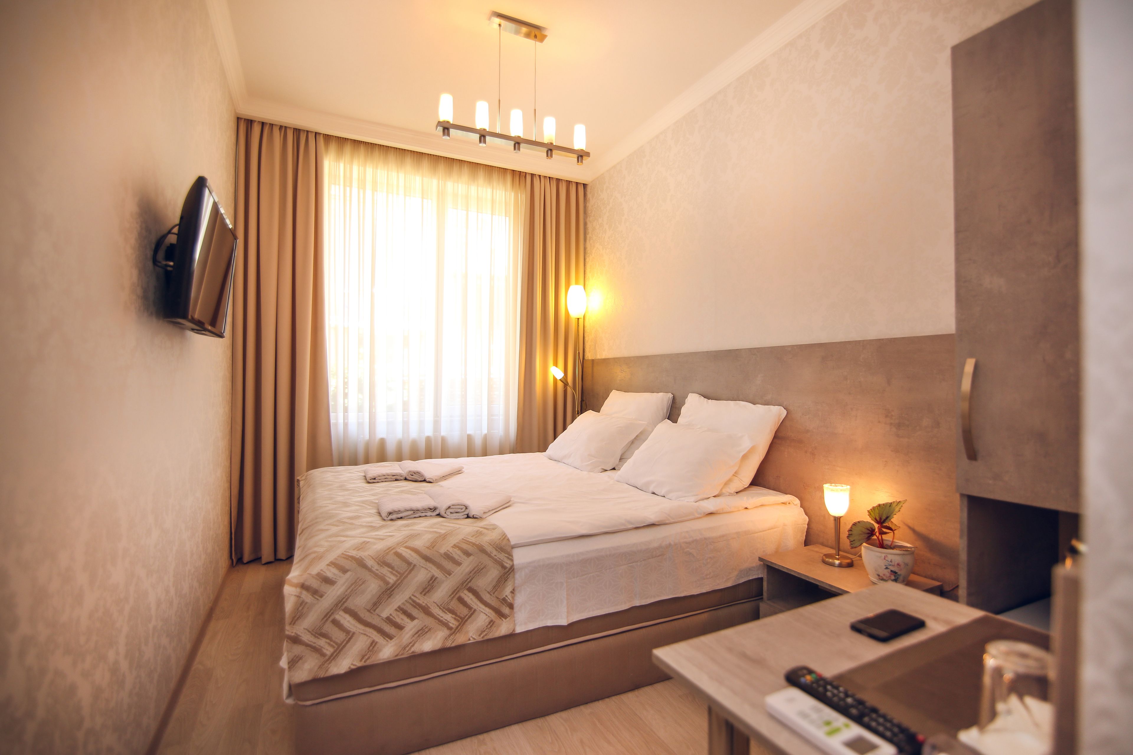 Una habitación de hotel con cama, mesita de noche, lámpara y televisión montada.