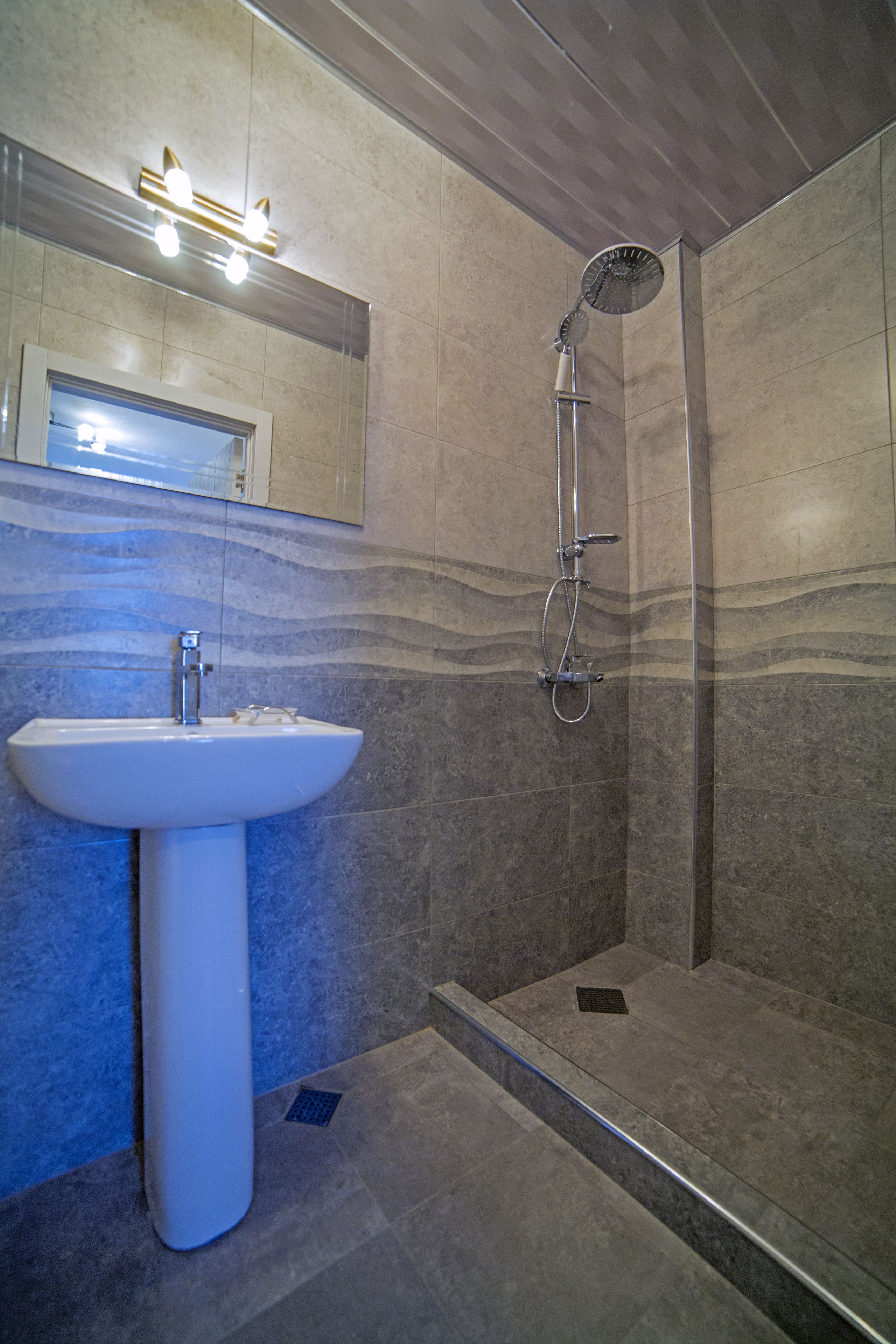 Une salle de bain avec un lavabo sur colonne, une douche et un miroir au-dessus du lavabo.