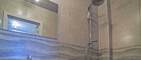 A bathroom with a pedestal sink, a shower, and a mirror above the sink.