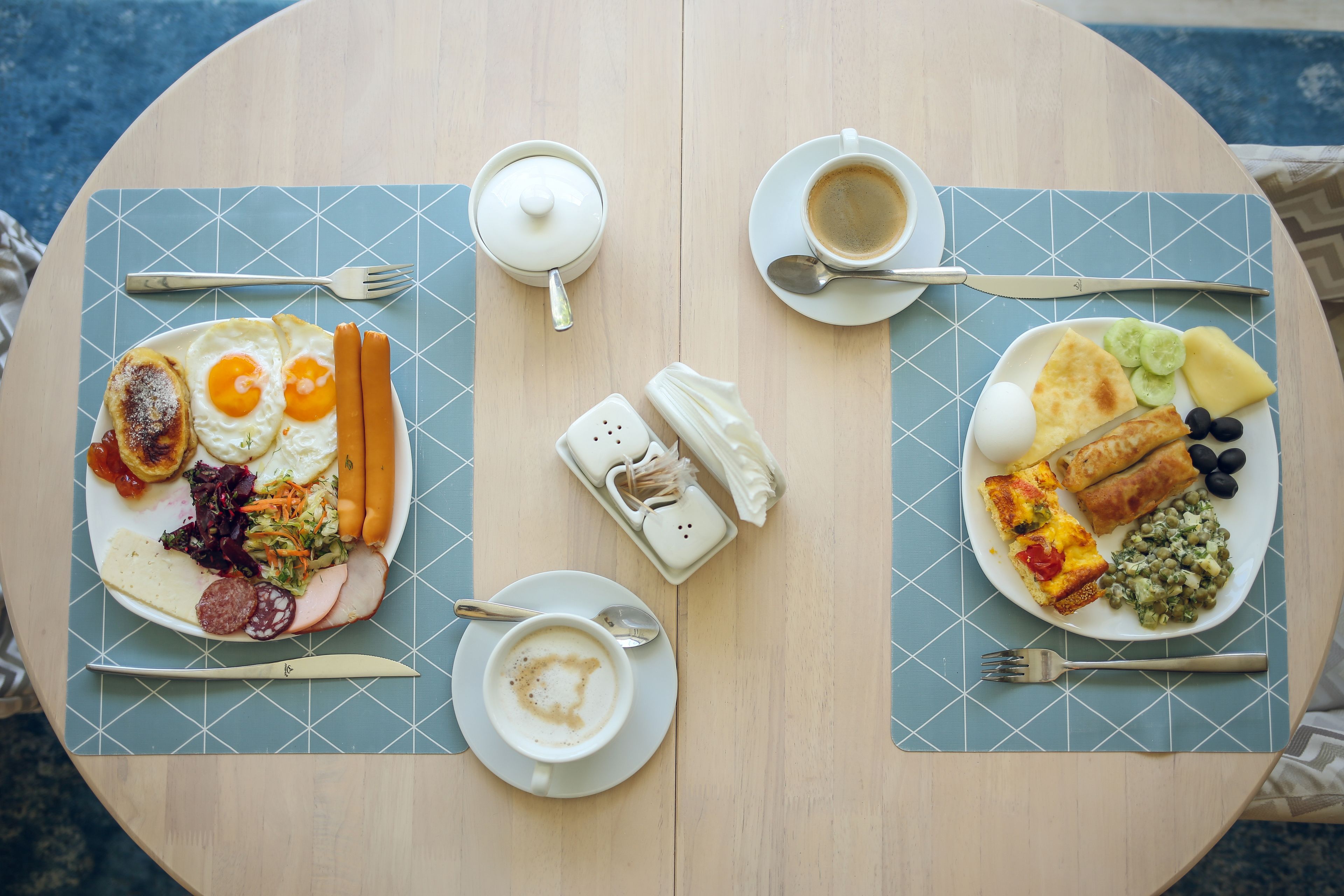 Ein runder Tisch mit zwei Frühstückstellern, einer Kaffeetasse und einem Salz- und Pfefferset.