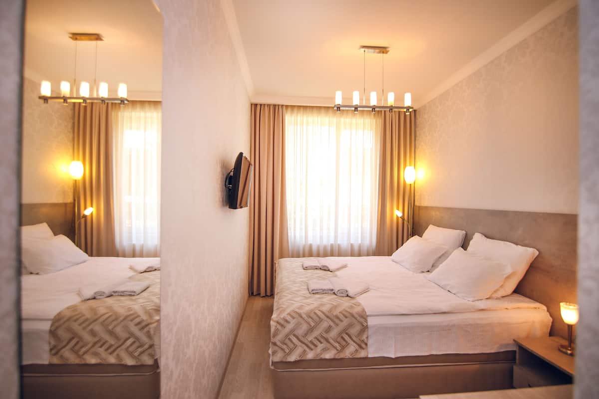 A hotel room with two beds, a mirror, a nightstand, and a chandelier.
