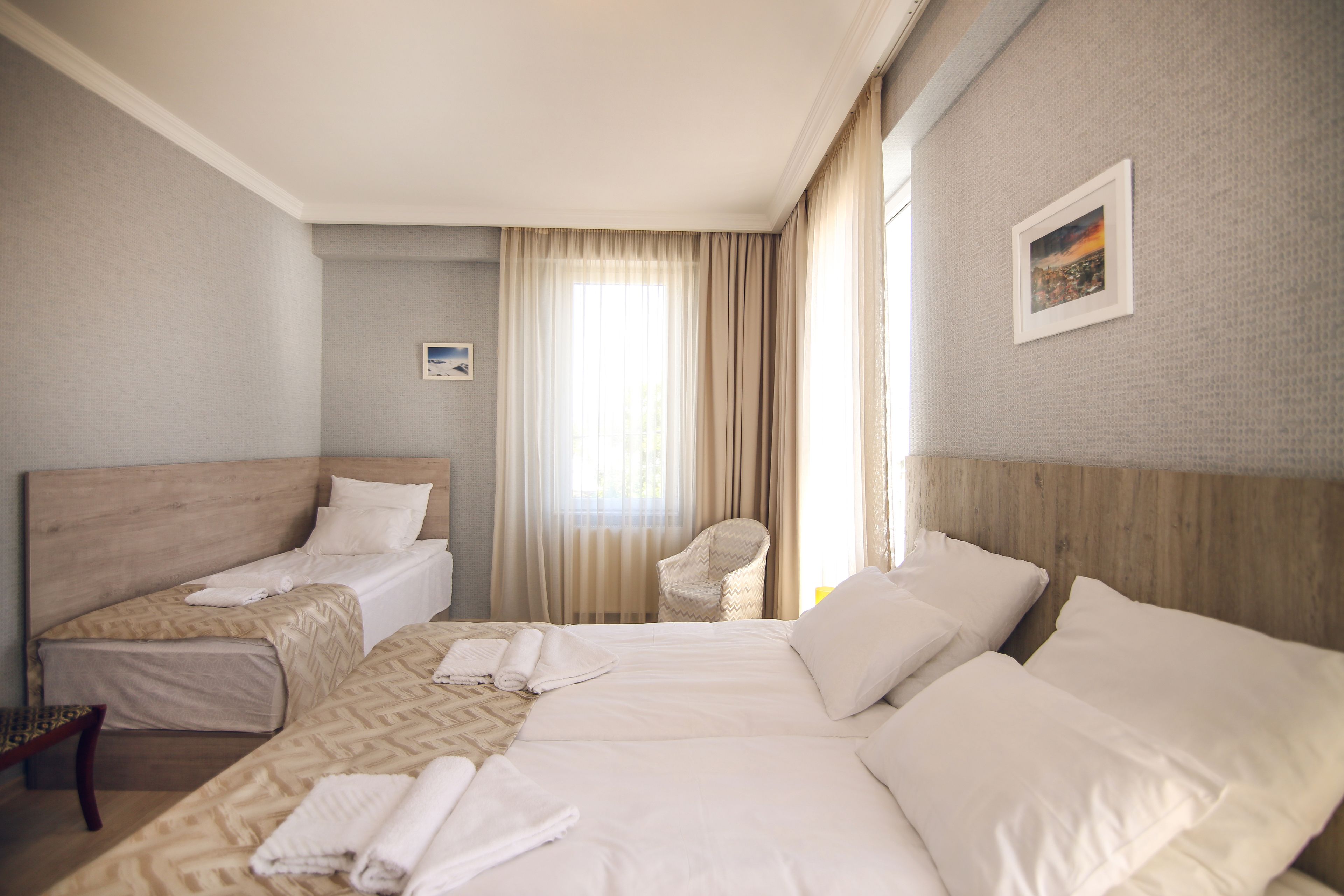 A hotel room with two beds, a chair, and a window with curtains.