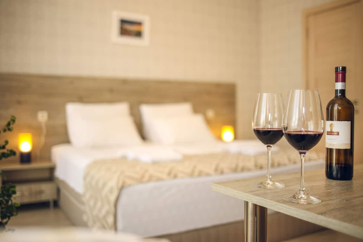 A bedroom with a bed, bedside lamps, and a table with two wine glasses and a bottle.