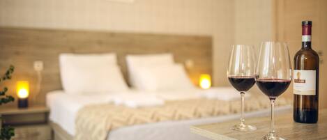 Un dormitorio con cama, lámparas de noche y una mesa con dos copas de vino y una botella.