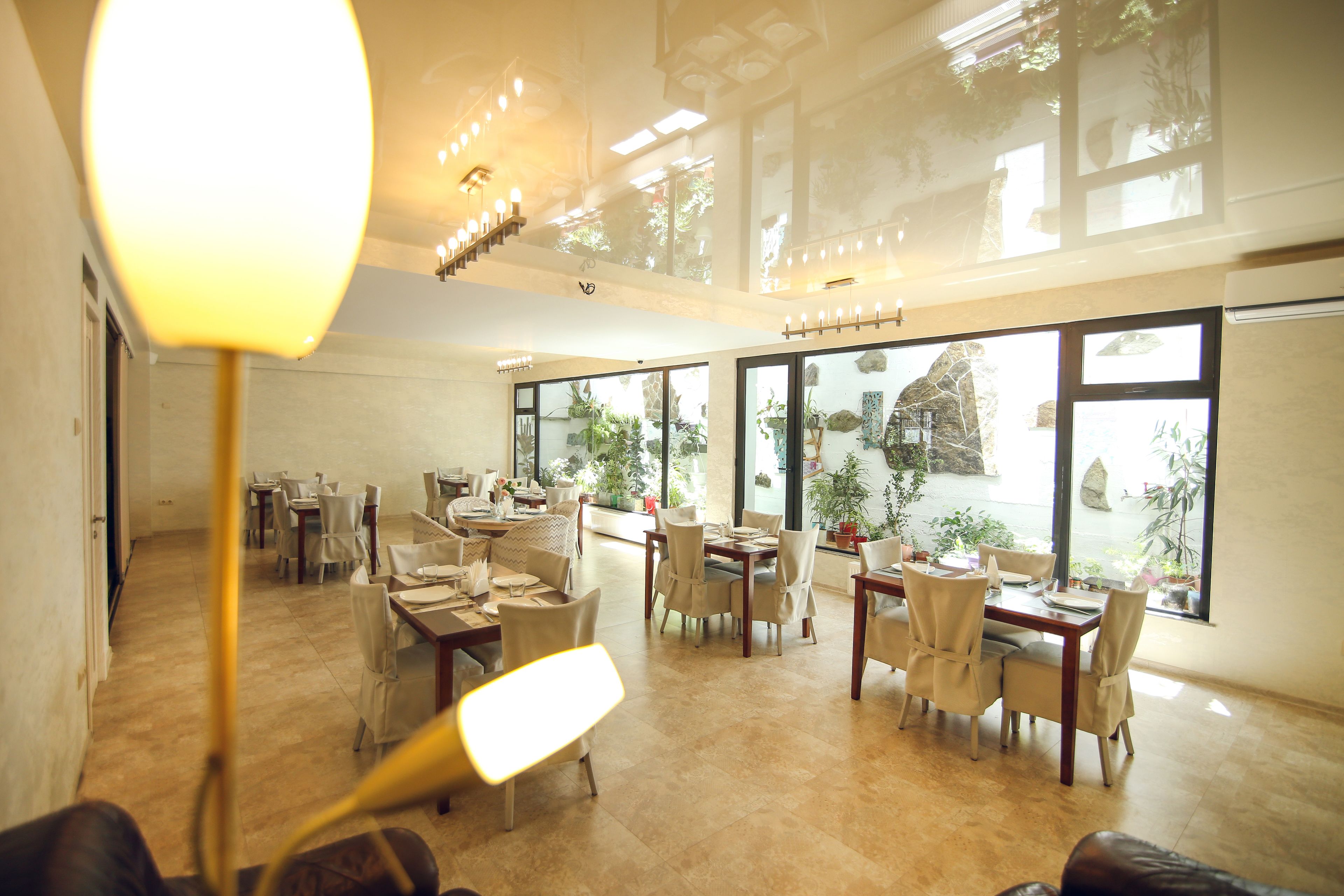 Un vaste espace dédié à la salle à manger, avec de nombreuses tables et chaises, de grandes fenêtres ornées de plantes et un lustre moderne.