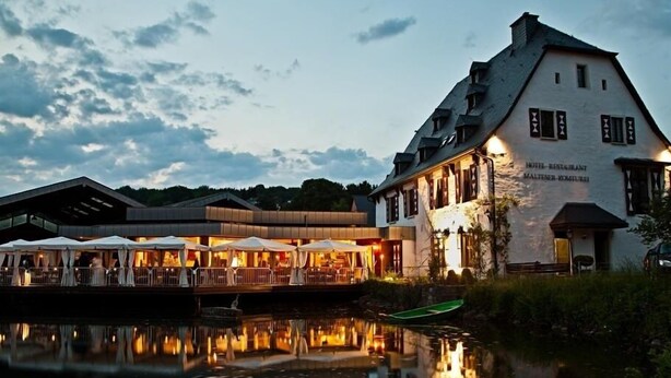 A riverside hotel with outdoor seating and a reflection in the water. - Malteser Komturei Hotel / Restaurant (Bergisch Gladbach)