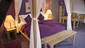 A bedroom with a four-poster bed, two bedside tables with lamps, a wooden bench, a chair, and a wardrobe. - Malteser Komturei Hotel / Restaurant (Bergisch Gladbach)