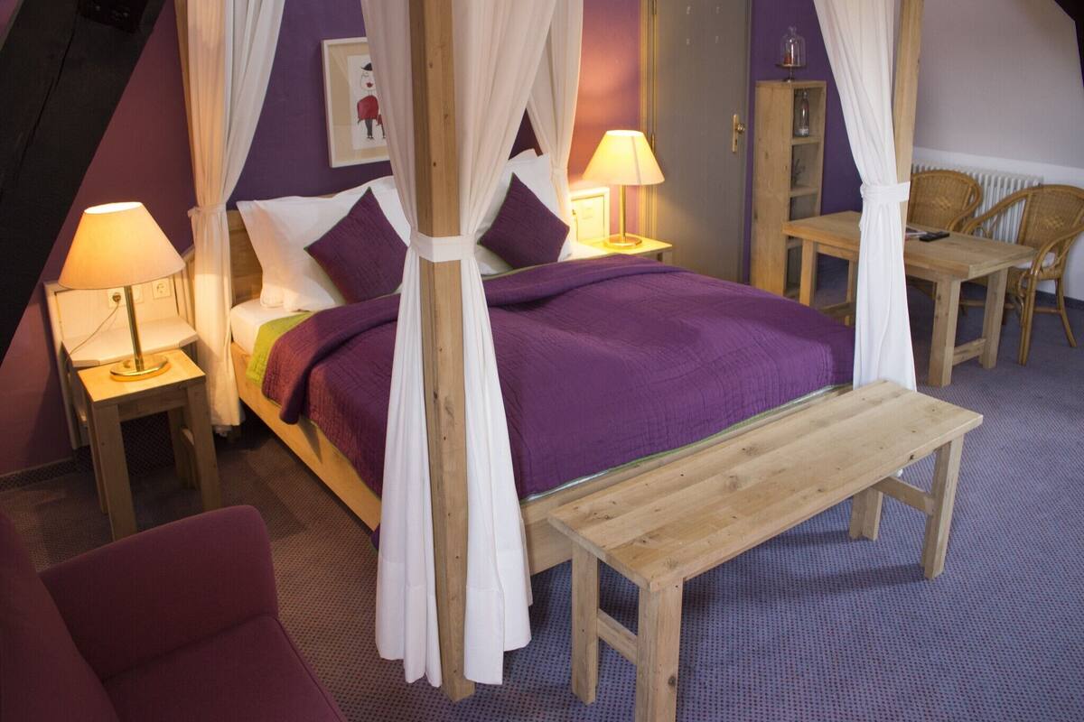 Une chambre à coucher avec un lit à baldaquin, deux tables de chevet avec des lampes, un banc en bois, une chaise et une armoire.