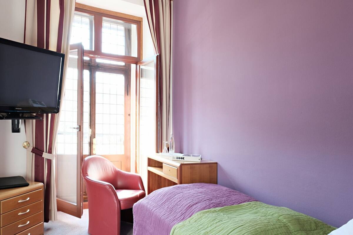 Une chambre d’hôtel équipée d’un lit, d’un bureau, d’une chaise, d’une télévision et d’une fenêtre avec des rideaux.
