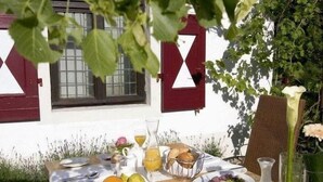 An outdoor dining table with various fruits, bread, and beverages, set against a white building with red shutters. - Malteser Komturei Hotel / Restaurant (Bergisch Gladbach)