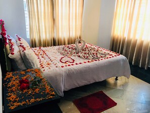 A bed with rose petals and a swan-shaped towel arrangement, a red rug, and a small table with orange flowers. - Hotel Suite Sadaf (Cox's Bazar)