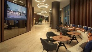 Eine moderne Lobby mit einem großen Fernsehbildschirm, runden Deckenleuchten und einer Sitzecke mit Sofas und Tischen.