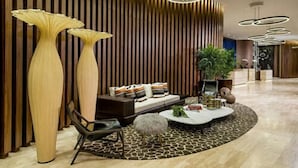 Eine moderne Lobby mit einer Wand aus Holzleisten, einer Couch mit Kissen, einem Couchtisch und großen Vasen.