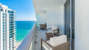 Ein Balkon mit Korbmöbeln und einem Tisch, der Blick auf einen Strand und das Meer freigibt.