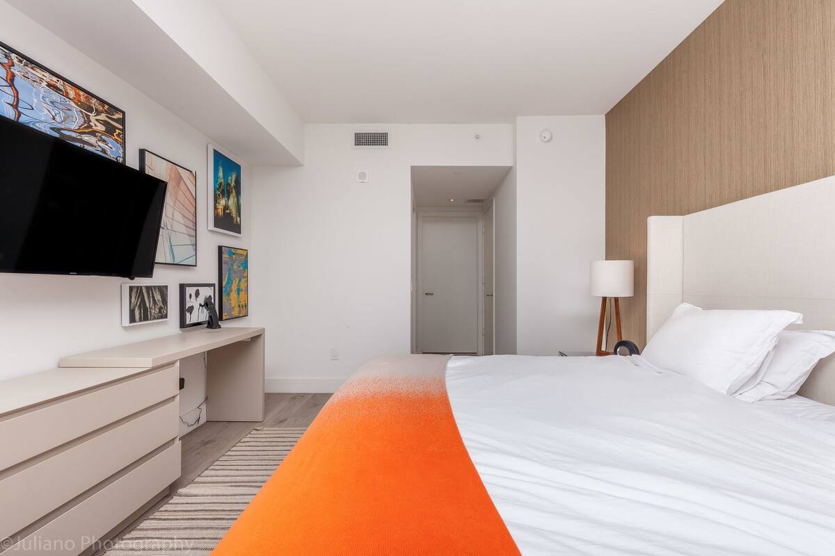 A modern bedroom with a bed, a TV mounted on the wall, a desk, and artwork.