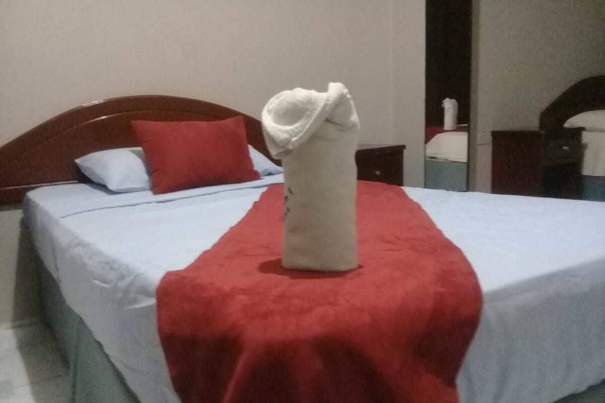 A bed with a red blanket and a white towel arranged on it.