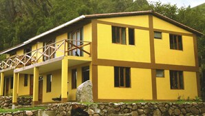 Un bâtiment jaune à deux étages, doté d’un balcon, d’un mur en pierre et d’un grand rocher au premier plan.