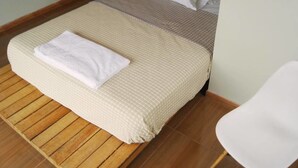 Un lit bien fait, surmonté d’une serviette blanche, un plancher en bois et une chaise blanche à droite.