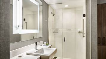 A modern bathroom with a large mirror, two sinks, a shower, and a walk-in closet.