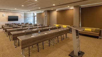 Une salle de conférence équipée de plusieurs tables, de chaises, d’un pupitre et d’un grand écran.