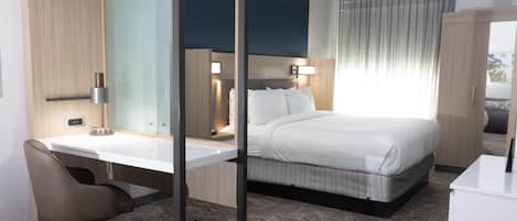 A modern hotel room with a bed, a desk, a chair, a mirror, and a window with curtains.