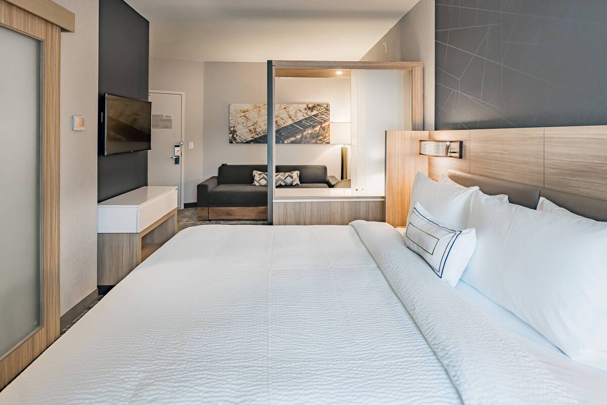 A modern hotel room with a large bed, a TV, a sofa, and a desk.