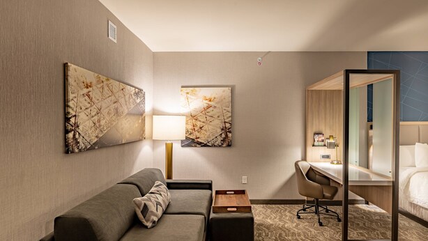 A hotel room with a sofa, a desk, a chair, a bed, and two wall-mounted artworks. - SpringHill Suites by Marriott Dallas McKinney/Allen (McKinney)