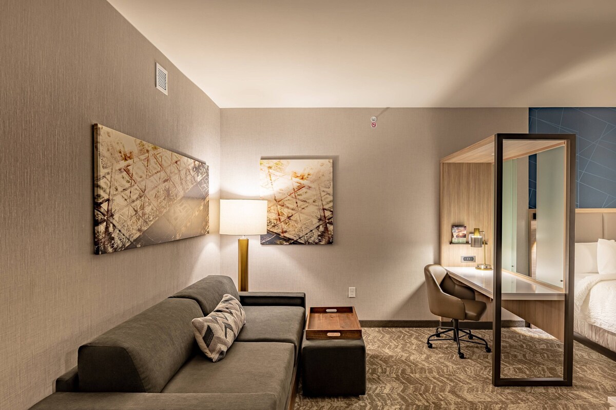 A hotel room with a sofa, a desk, a chair, a bed, and two wall-mounted artworks.