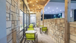 Un espace extérieur aménagé en terrasse, avec des murs en pierre, des chaises vertes et des tables.