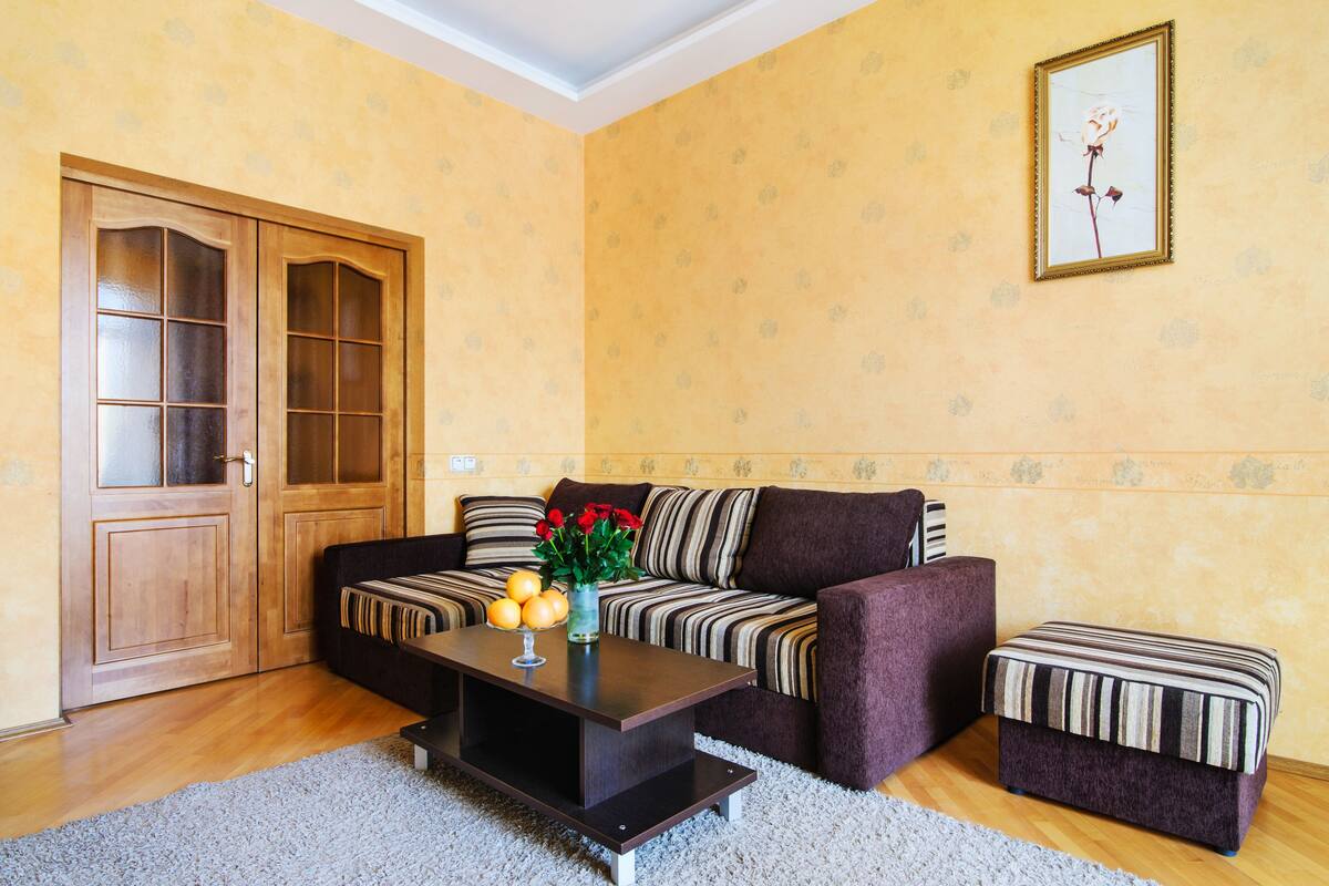 A living room with a sofa, a coffee table with fruit, a door, and a framed picture on the wall.