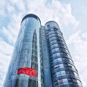 A tall, modern skyscraper with reflective glass facades and a prominent red flag at the base. - Relaxed Season Hotel (Shenzhen)
