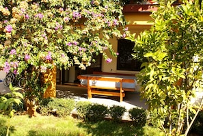 A bench in a garden with a yellow building in the background.
