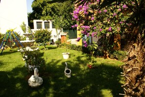A garden with a swing set, a bird bath, and flowering plants.