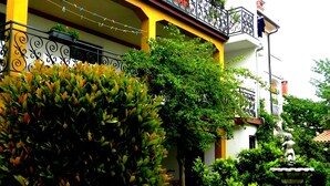 A building with a yellow facade, black wrought iron balcony railings, and a garden with a fountain and various plants. - Accommodation Stosic (Rovinj)