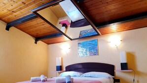 A bedroom with a wooden ceiling, a bed with pink and white bedding, two wall-mounted speakers, and a framed picture on the wall. - Accommodation Stosic (Rovinj)