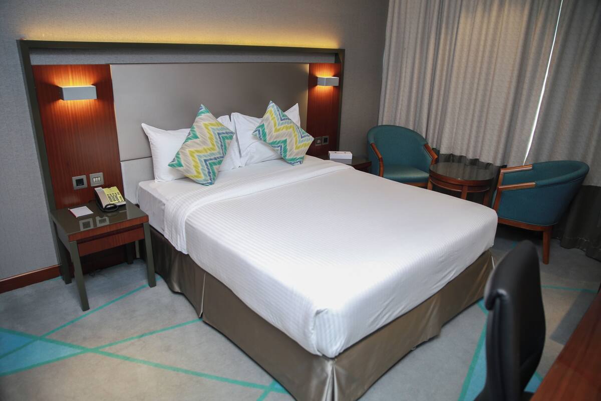 A hotel room with a large bed, two bedside tables, a desk, a chair, and a small table.