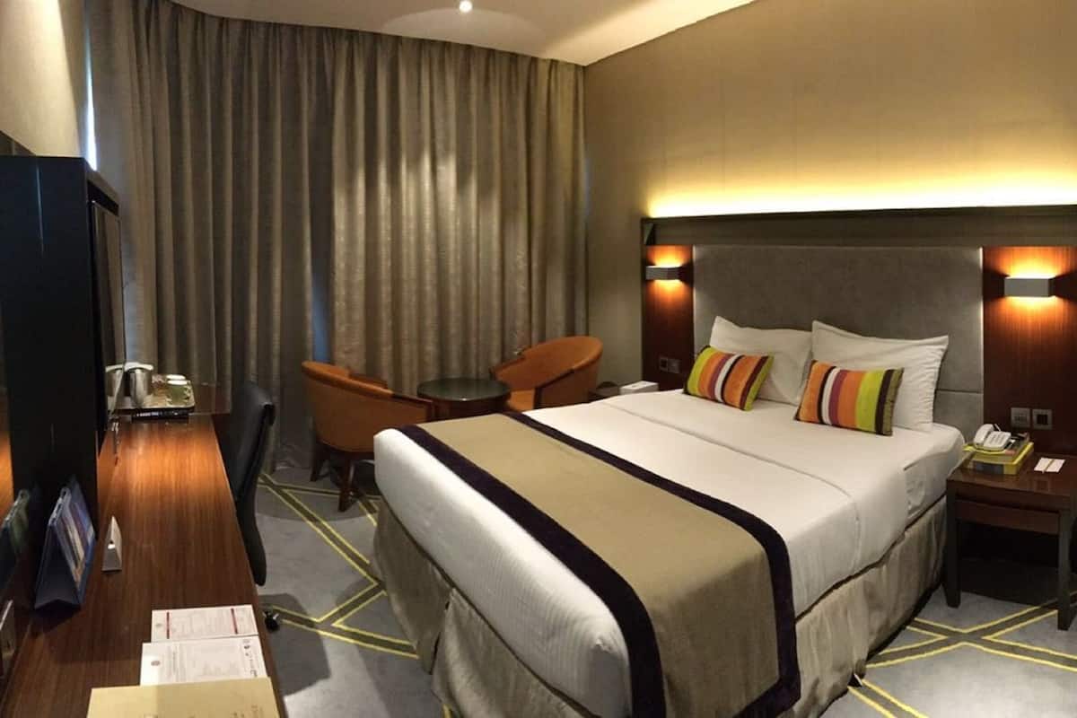 A hotel room with a large bed, a desk with a chair, a telephone, and a television.