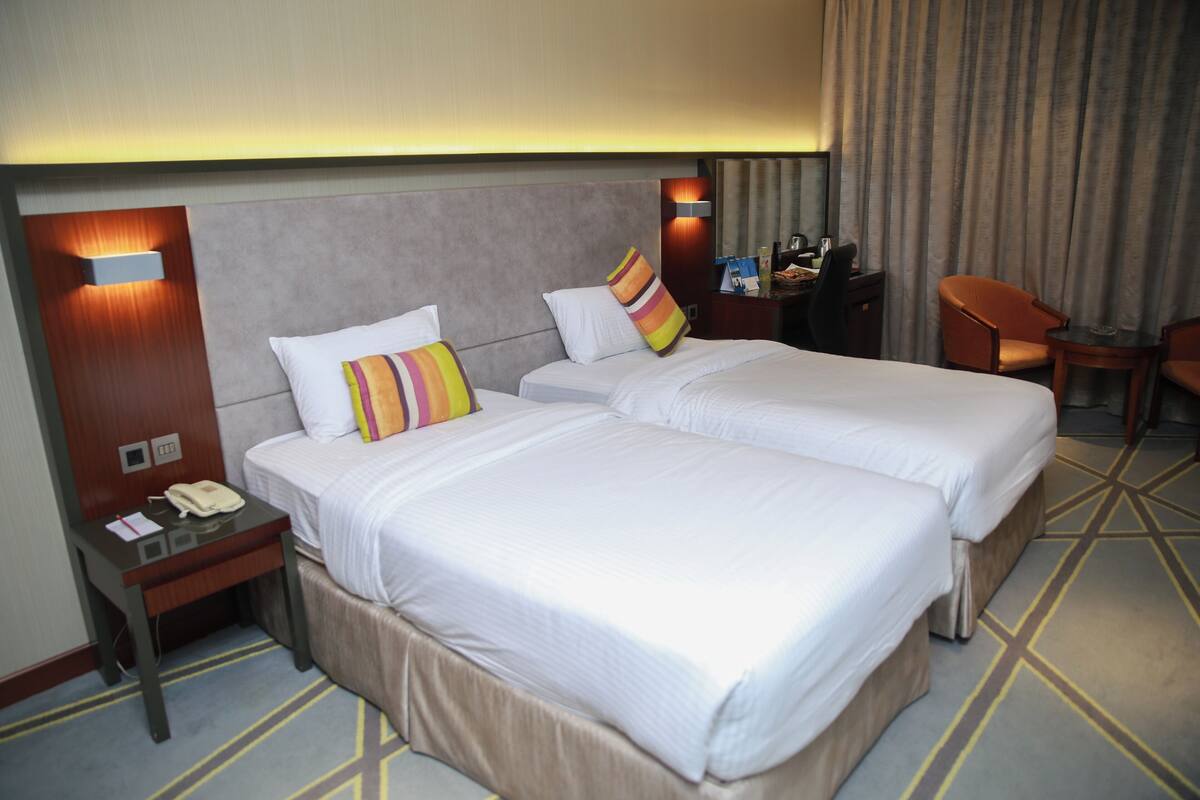 A hotel room with two beds, a desk, a chair, and a nightstand.